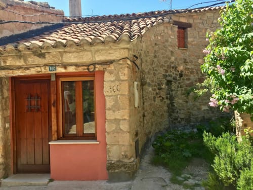 Entrada rústica de piedra en Rustikalpuente con puerta roja, techo de tejas arqueado y muros cubiertos de hiedra en España