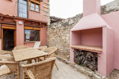 Patio rosa con sillas de mimbre, mesa de madera y chimenea integrada en el apartamento Rustikalpuente, España
