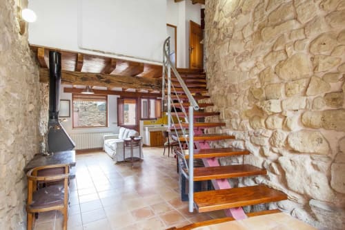 Interior del apartamento Rustikalpuente con muros de piedra, escaleras de madera, chimenea y vigas rústicas