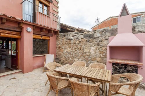 Patio del apartamento Rustikalpuente con mesa de comedor, sillas de mimbre, chimenea y muros de piedra