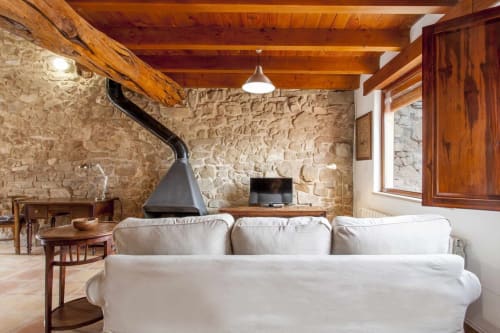 Acogedora sala de estar rústica con paredes de piedra vista, vigas de madera, sofá blanco, chimenea y muebles de madera