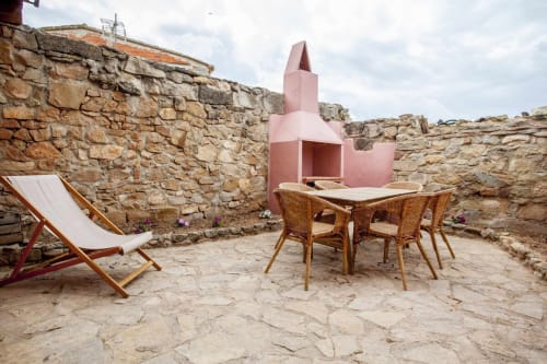 Patio rústico con chimenea rosa, mesa de comedor de madera, tumbona y muros de piedra en el apartamento Rustikalpuente