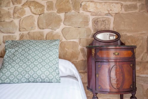 Dormitorio rústico con almohada de patrón verde, ropa de cama blanca y mesita de noche de madera con espejo