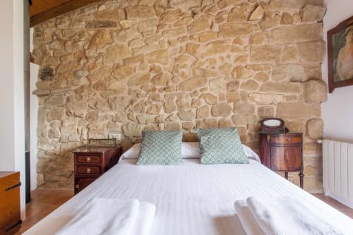 Dormitorio rústico de piedra con ropa de cama blanca y almohadas verdes en el apartamento Rustikalpuente en España