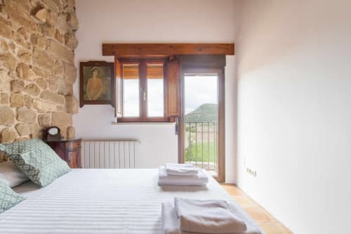 Luminoso dormitorio en Rustikalpuente con pared de piedra, viga de madera, radiador moderno y vistas a la montaña desde el balcón