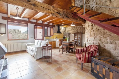 Apartamento rústico y espacioso en Rustikalpuente con vigas de madera, muros de piedra, sofá crema, sillones de rayas rojas y amarillo