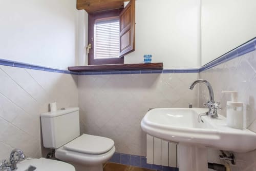 Baño del apartamento Rustikalpuente con lavamanos pedestal blanco, inodoro, moldura de azulejos azules y ventana con persianas de madera