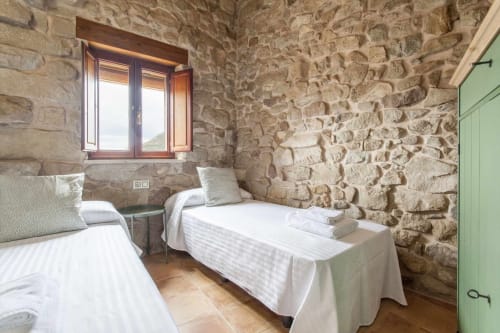 Dormitorio doble con muros de piedra rústica y vigas de madera en el apartamento Rustikalpuente, España