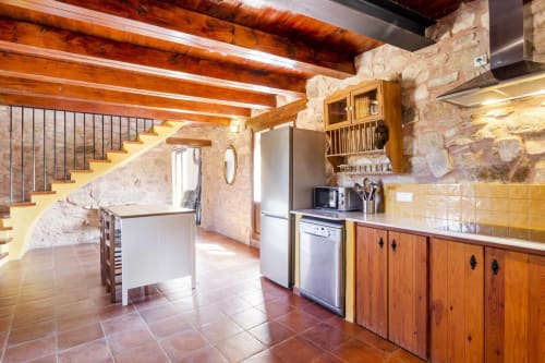 Acogedor apartamento de cocina rústica con vigas de madera vista, muros de piedra, baldosas de terracota y escalera en España