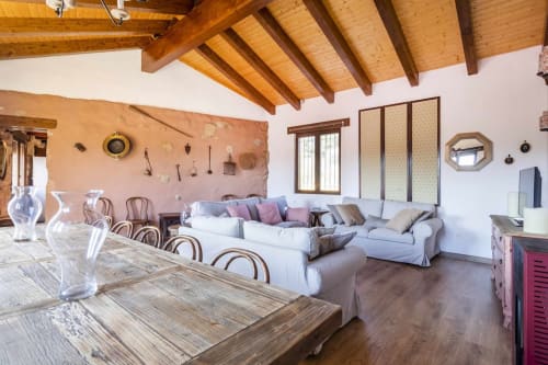 Amplio apartamento rústico en Rustikalpuente con vigas de madera vista, sofá blanco, mesa de comedor y pared acentuada en terracota.