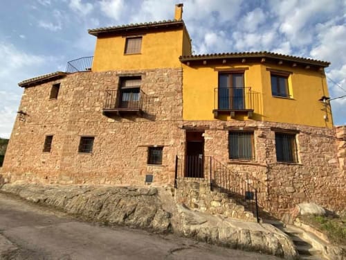 Entrada del apartamento Rustikalpuente con fachada de piedra y sección superior amarilla, arquitectura rural española tradicional