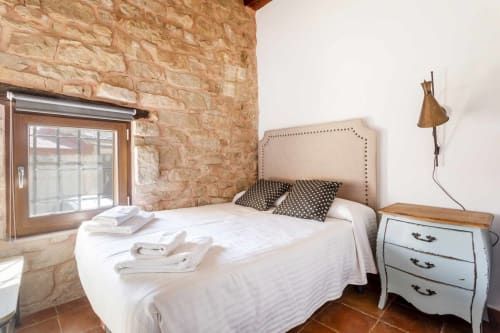 Dormitorio rústico de piedra en apartamento Rustikalpuente con piso de terracota, cama con cabecero arqueado y puerta de madera que se abre a