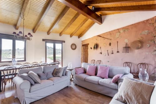 Amplio salón rústico con vigas de madera, sofás blancos, detalles en rosa y pared de terracota