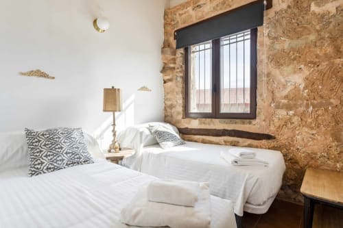 Dormitorio doble en Rustikalpuente con muros de piedra rústica, ropa de cama blanca y ventana con vistas al campo español