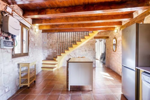 Interior rústico en Rustikalpuente con vigas de madera vista, azulejos de barro, muros de piedra y escaleras amarillas