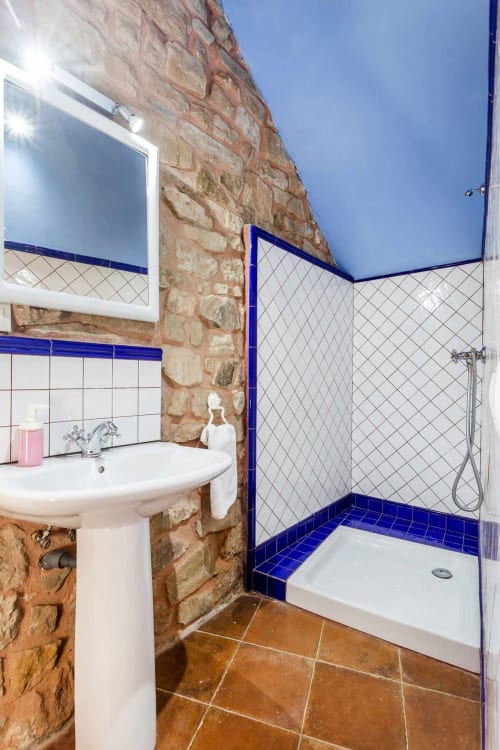 Baño moderno en apartamento Rustikalpuente con pared de piedra rústica, detalles en azulejos azules, lavamanos pedestal y ducha abierta