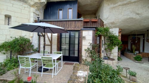 Garden terrace at Les Troglos de Beaulieu with white furniture under black umbrella, ivy-covered stone building
