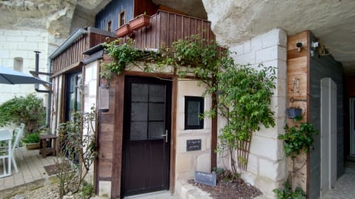 Stone-built entrance of Le Logis Du Gardien at Les Troglos de Beaulieu, featuring dark wooden door with ivy and climbing