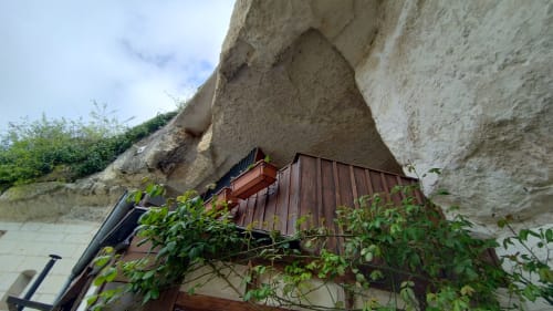 Troglodyte dwelling carved into stone cliff at Les Troglos de Beaulieu, with wooden door and lush greenery
