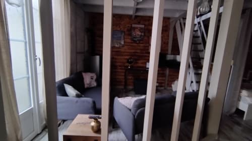 Cozy bedroom with grey upholstered bed and seating area, wooden accent wall, and garden view at Les Troglos de Beaulieu