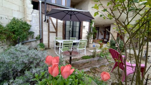 Charming courtyard garden at Les Troglos de Beaulieu with red tulips, patio dining area, black umbrella, and stone buildings.