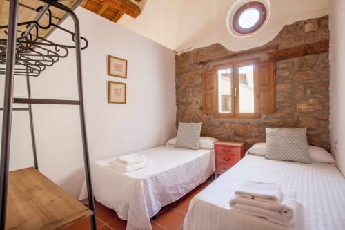 Dormitorio doble con muros de piedra rústica, muebles de madera y luz natural en el apartamento Rustikalpuente en España.