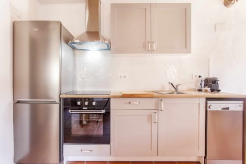 Cocina moderna en apartamento Rustikalpuente con electrodomésticos de acero inoxidable, gabinetes beige y azulejos de metro blanco