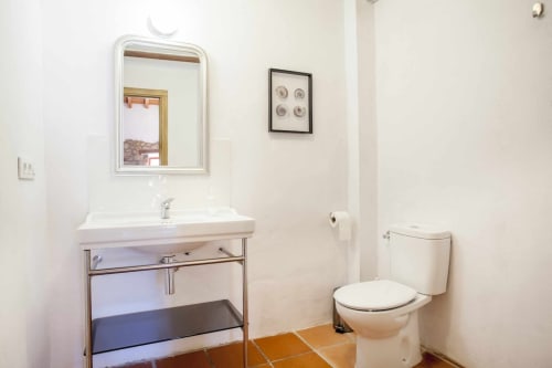 Baño limpio en apartamento Rustikalpuente con lavabo blanco, espejo, inodoro y suelo de baldosas de barro en España