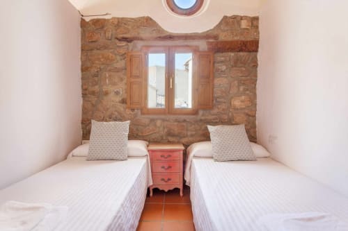 Dormitorio doble con muros de piedra y ventana de madera en la casa rural Rustikalpuente en España