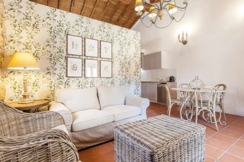 Sala de estar del apartamento Rustikalpuente con papel pintado botánico, sofá color crema, muebles de mimbre y cocineta en España
