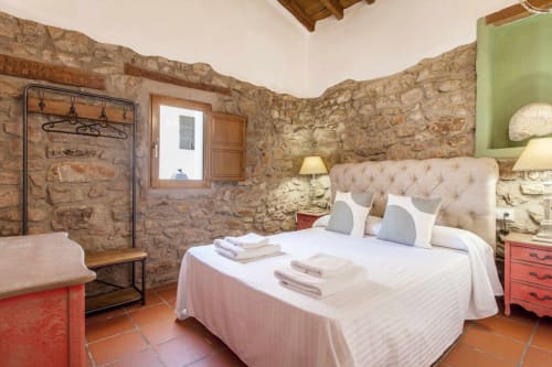 Dormitorio rústico en Rustikalpuente con vigas de madera, suelo de terracota, cabecero capitoné crema y detalles rojos tradicionales