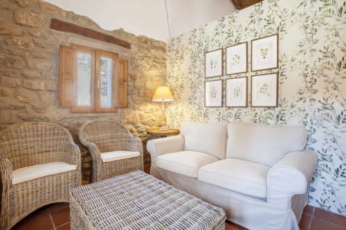 Acogedor apartamento en Rustikalpuente con muebles de mimbre, sofá blanco, papel tapiz botánico y paredes de piedra rústica en España.