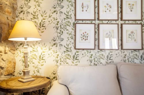 Acogedor rincón de apartamento en Rustikalpuente con papeles pintados botánicos, cuadros de flores enmarcados y una lámpara de mesa resplandeciente junto a gris