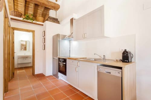 Cocina moderna en apartamento Rustikalpuente con muebles blancos, vigas de madera, electrodomésticos acero inoxidable y terracota