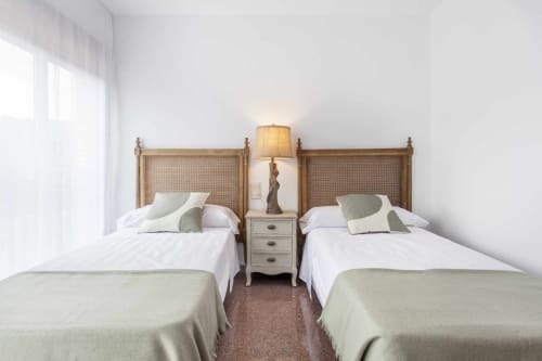 Dormitorio doble en apartamento Rustikalpuente con cabeceros de ratán, ropa de cama blanca y decoración neutral