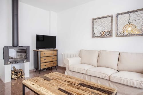 Sala de estar moderna en Rustikalpuente con sofá crema, mesa de café de madera, chimenea, TV y arte decorativo en pared.