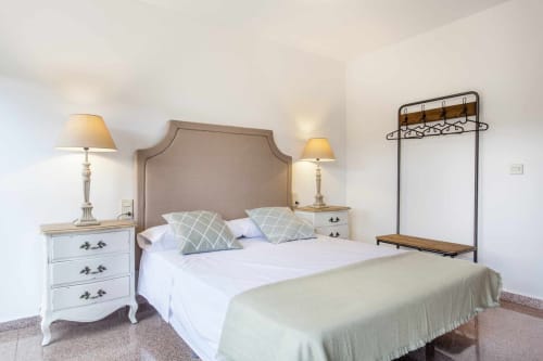 Dormitorio elegante en apartamento Rustikalpuente con cabecero tapizado, mesillas blancas y estructura metálica decorativa.