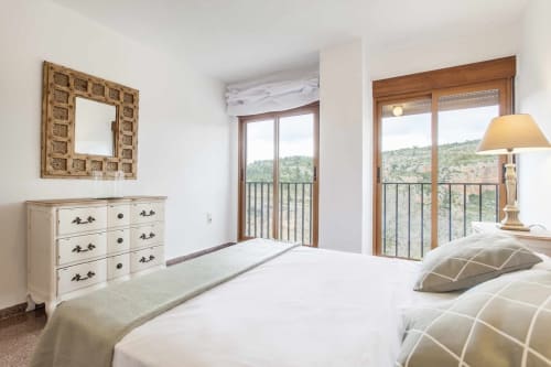 Dormitorio luminoso en apartamento Rustikalpuente con vistas al valle, muebles color crema y puertas balconeras de madera con vistas a las colinas
