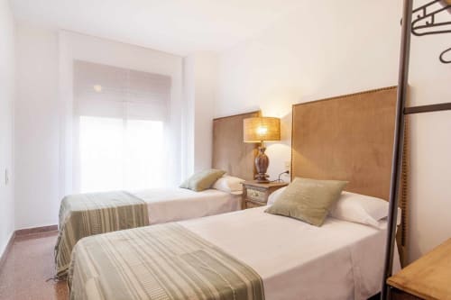 Dormitorio doble en apartamento Rustikalpuente con dos camas, cabeceros beige, lámpara y ventana luminosa