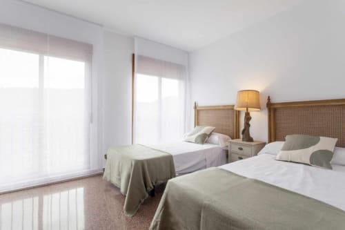 Dormitorio doble con cabeceros de madera, luz natural desde las puertas de balcón y decoración tradicional en el apartamento Rustikalpuente