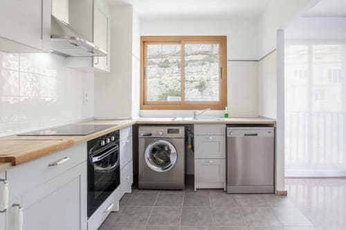 Cocina moderna blanca con electrodomésticos de acero inoxidable, marco de ventana de madera y pisos de azulejos grises en el departamento Rustikalpuente