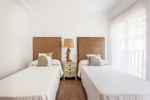 Dormitorio doble en apartamento Rustikalpuente con cabeceras color tostado, camas blancas y puertas hacia el balcón