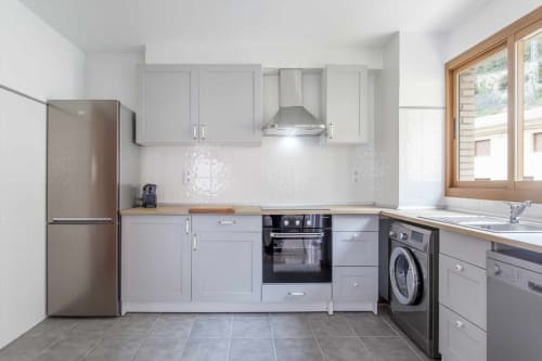Cocina moderna en apartamento Rustikalpuente con gabinetes blancos, electrodomésticos de acero inoxidable y luz natural