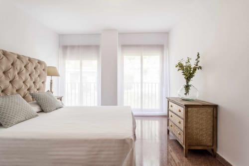Dormitorio luminoso y moderno en apartamento Rustikalpuente con cabecero tapizado, puertas de cristal al balcón y tocador de madera