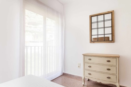 Dormitorio luminoso en Rustikalpuente con cómoda crema, puertas ventana al balcón y espejo rejilla en paredes blancas