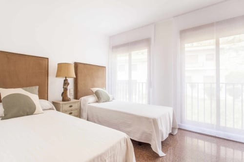 Luminosa habitación doble en apartamento Rustikalpuente con cabeceros beige, ropa de cama blanca y puertas al balcón con vistas a