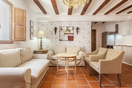 Acogedora sala de estar del apartamento Rustikalpuente con mobiliario crema, pisos de terracota, vigas de madera y cocina moderna