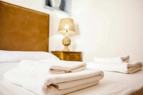 Dormitorio del apartamento Rustikalpuente con toallas cuidadosamente dobladas, lámpara dorada y cabecero de madera