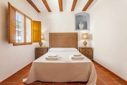 Dormitorio del apartamento Rustikalpuente con vigas de madera, suelo de terracota, cabecero de cuero tostado y lámparas gemelas en España