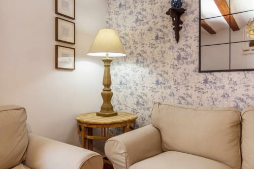 Zona de estar del apartamento Rustikalpuente con sillones crema, mesita de madera, lámpara de latón y papel tapiz azul toile, España